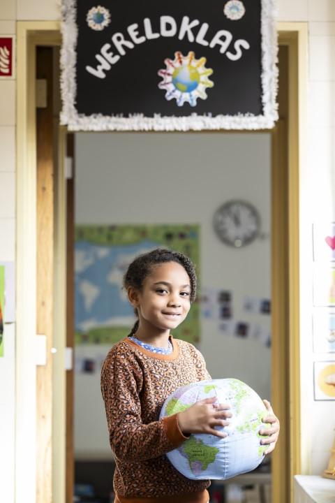 Meisje poseert met wereldbol in stedelijke basisschool De Octopus